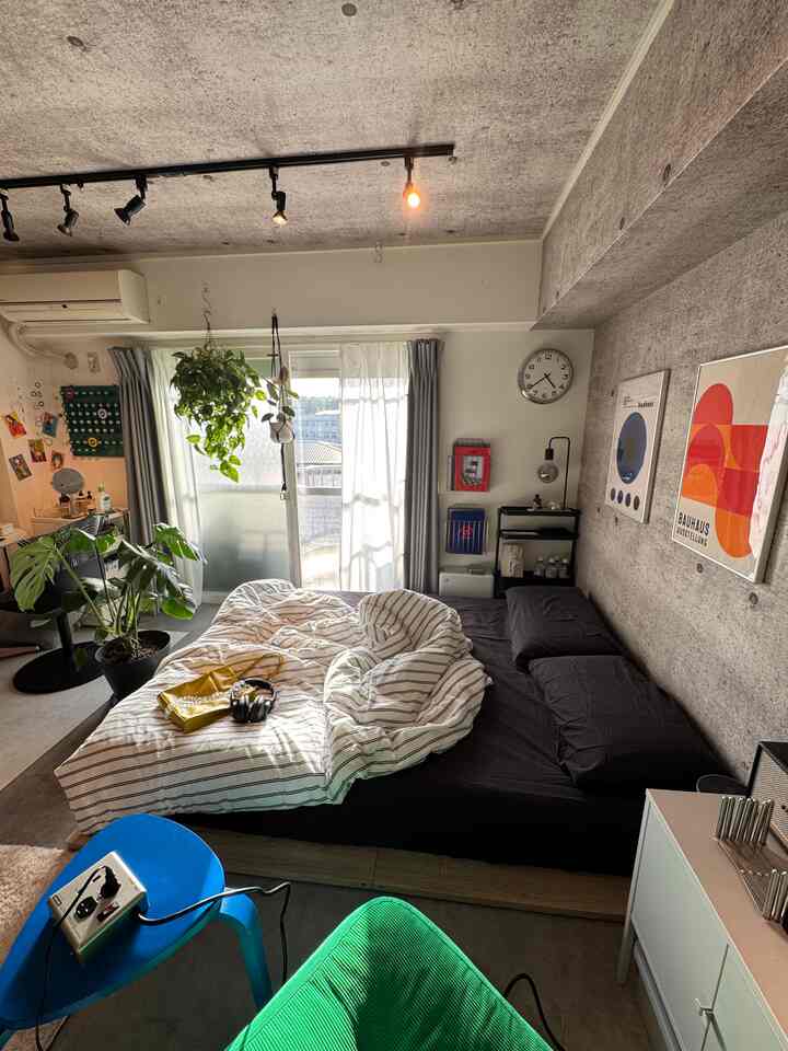コンクリート壁と天井に中型ベッドと緑の植物を配した、モダンでナチュラルな一人暮らしの寝室の雰囲気のあるインテリア