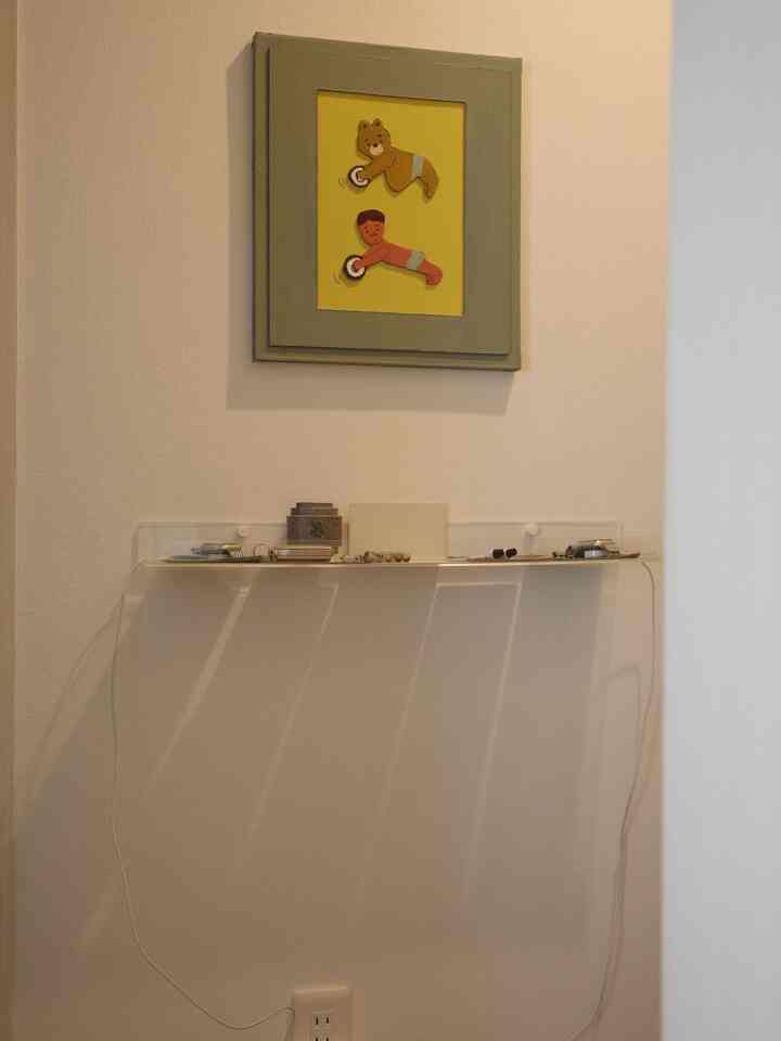 透明な棚と白い壁、かわいい絵が配置されたすっきりとした玄関スペース