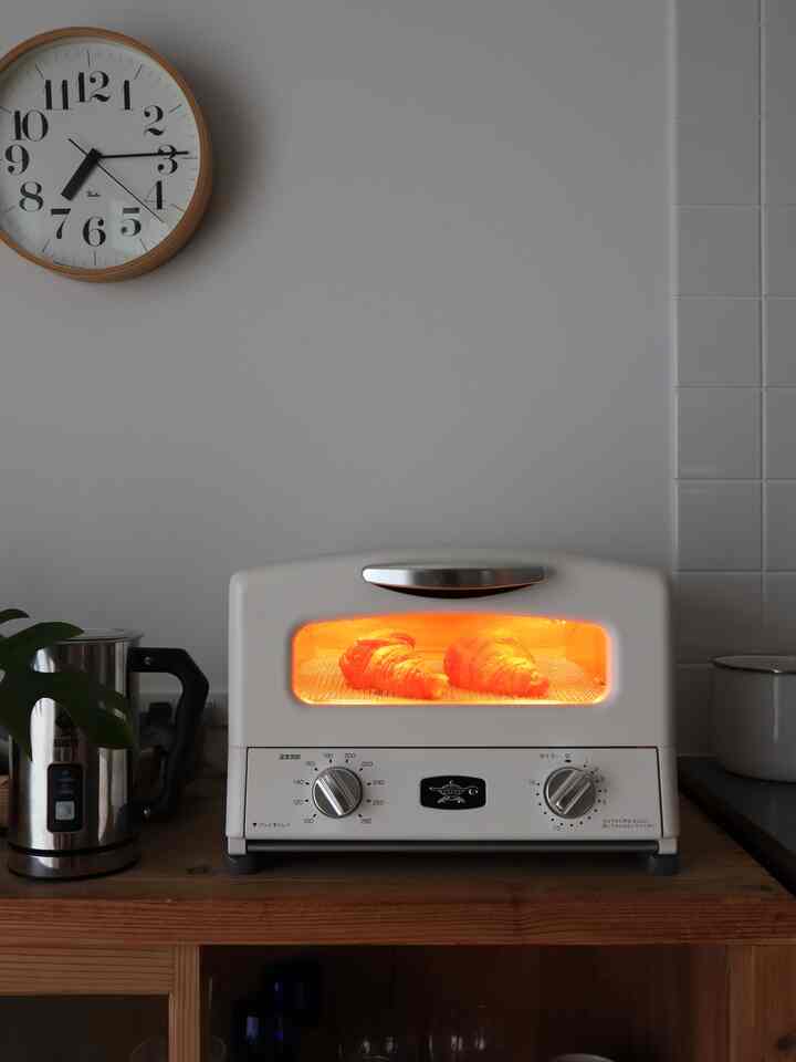 Natural color and white-brown toned kitchen featuring a toaster oven with baking croissants and a wall clock, warm atmosphere