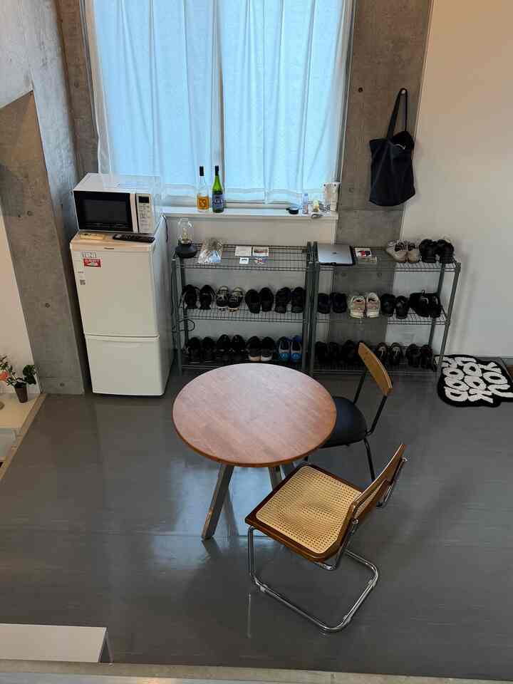 ナチュラルなブラウンとグレーの床が調和するコンパクトなダイニング、丸いダイニングテーブルとラタンチェアが配された印象的な空間