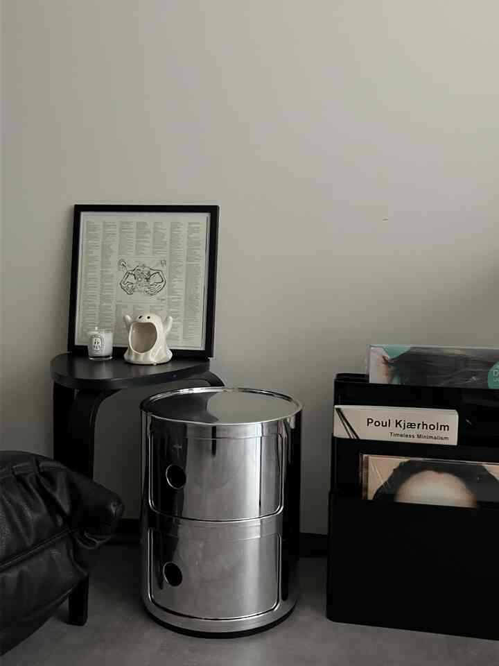 モノトーンのリビング空間、中央にシルバーの収納ユニット、左にサイドテーブルとレザーのチェアが配置されたミニマルで洗練されたインテリア