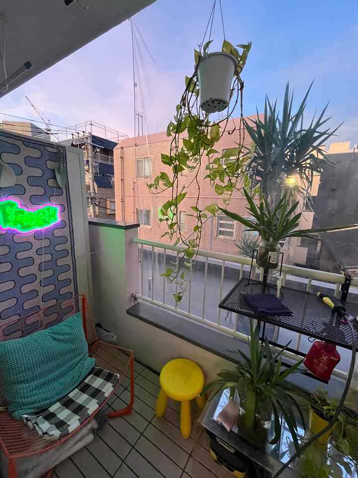 Small balcony with natural and yellow tones featuring lush plants, a cozy armchair, and a bright yellow stool