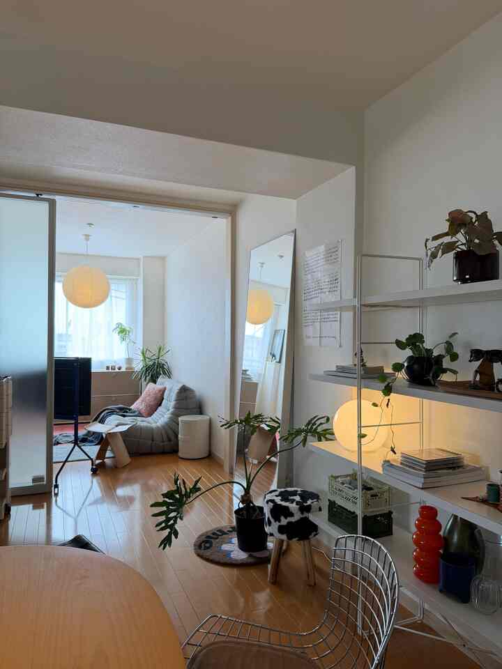 白い壁と木目調の床が特徴のミッドセンチュリーモダンリビング、グレーのソファ、大きな鏡、ペンダントライトが配置された雰囲気のある空間