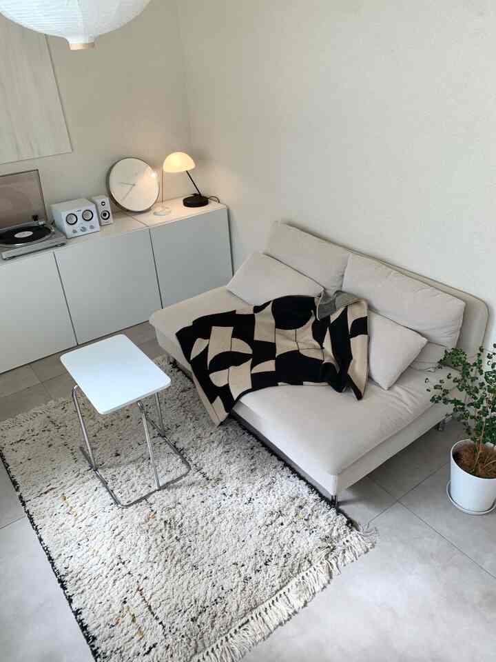 モノトーンのナチュラルモダンなリビングルーム、ベージュのソファに黒の幾何学模様のブランケットと白いサイドテーブルが配置された落ち着いた空間