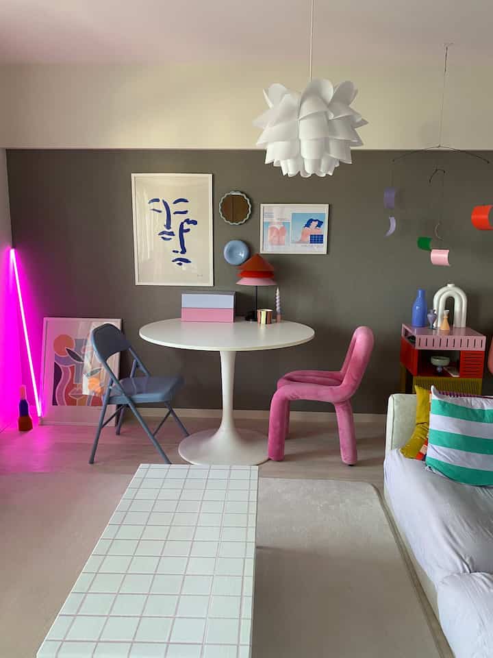 グレーの壁紙と白い円形テーブル、ピンクの椅子、多彩なインテリア小物が配置された北欧風のリビング兼ダイニング空間