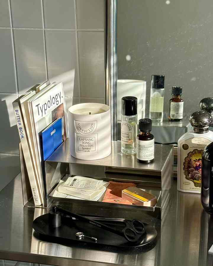 白とシルバーのトーンのデスク空間、ステンレスデスクオーガナイザーやキャンドル、本が整然と配置されたモダンなインテリア