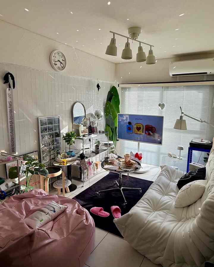 Minimal and cozy living room in white and pink tones, featuring sofa, bean bag, and black rug as key elements