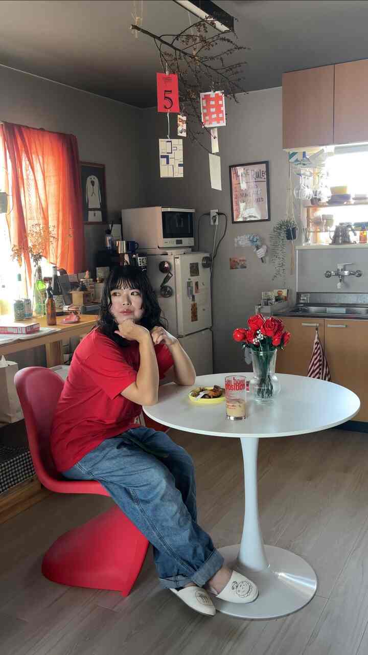 赤と白の調和が美しい1LDKのキッチン兼ダイニングルーム、丸いダイニングテーブルと赤い椅子が配置された温かみのあるモダンな空間