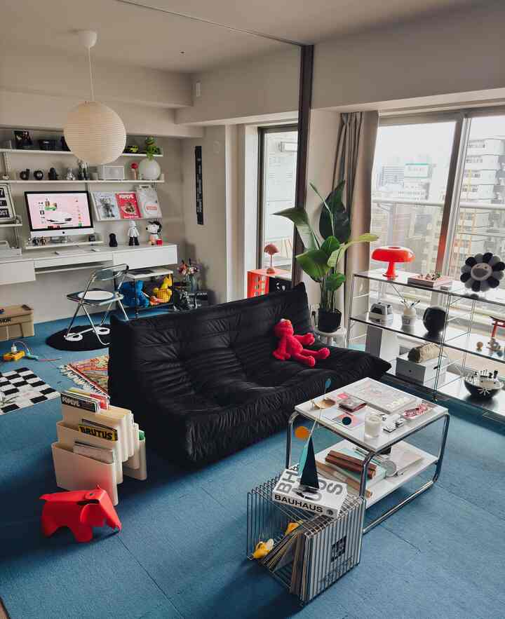 Modern living room with a black sofa and blue carpet, featuring a bookshelf and home office area on the wall, creating a cozy atmosphere