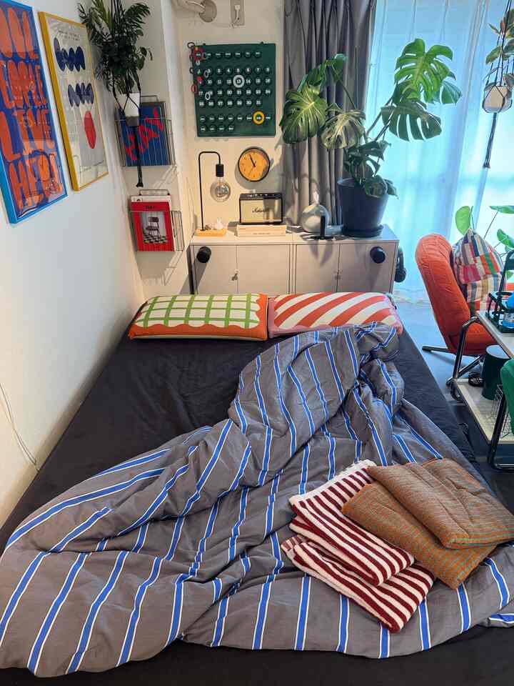 Natural-toned bedroom featuring a single bed with colorful pillows and prominent greenery, creating a cozy atmosphere