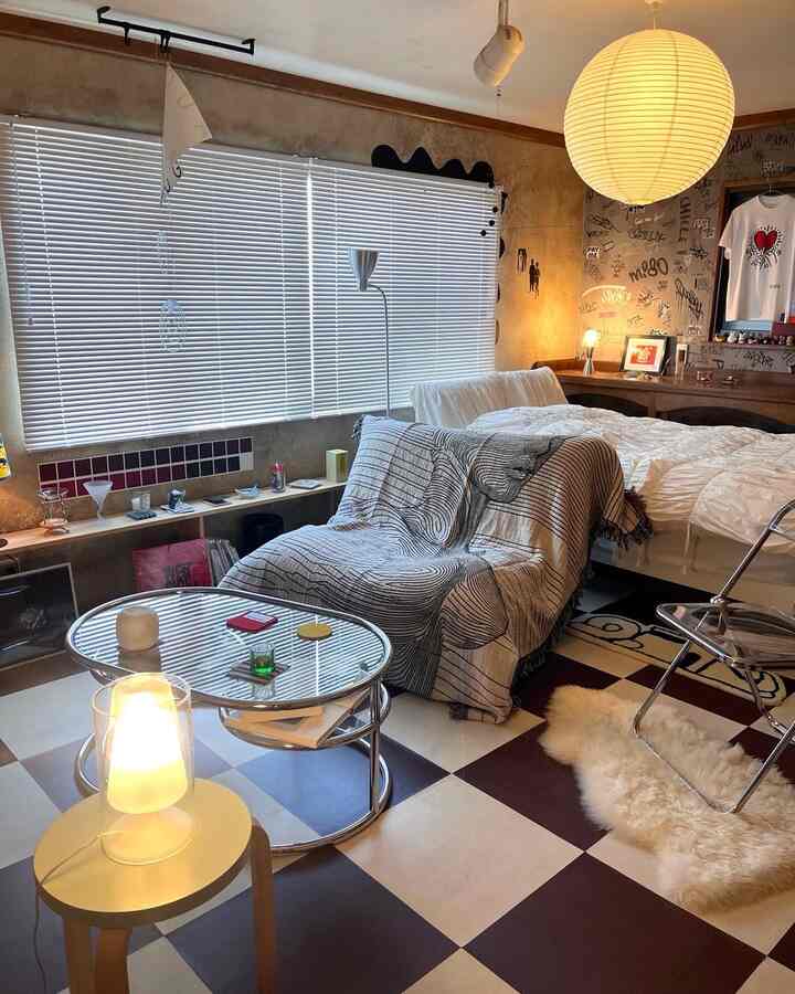A white and brown toned studio apartment living room featuring a sofa with throw blanket, modern lighting, and checker-patterned floor