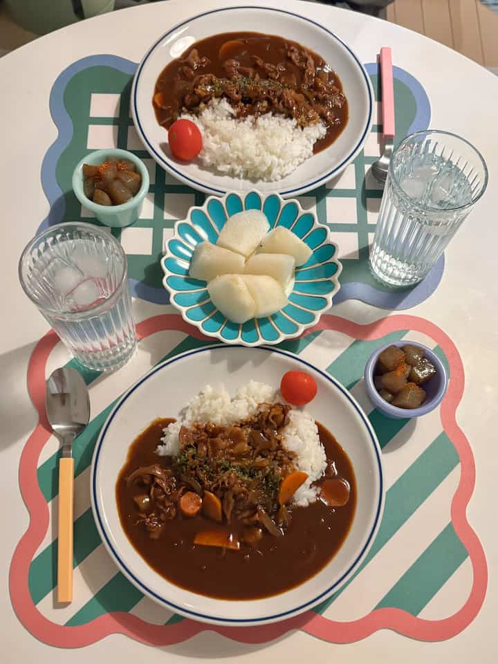 ナチュラルカラーの1LDKダイニングテーブルにカラフルなランチョンマットと2皿のハヤシライスが配された雰囲気のあるインテリア