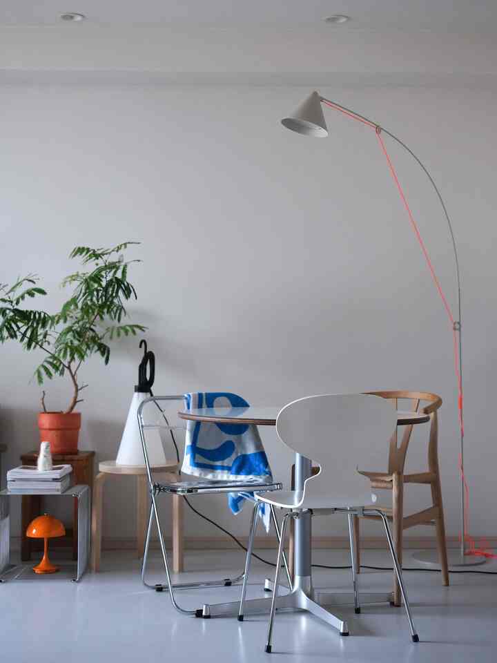 明るい色調の北欧リビング、円形テーブルと様々な椅子、青いブランケットとフロアランプが配置された清潔感のある空間