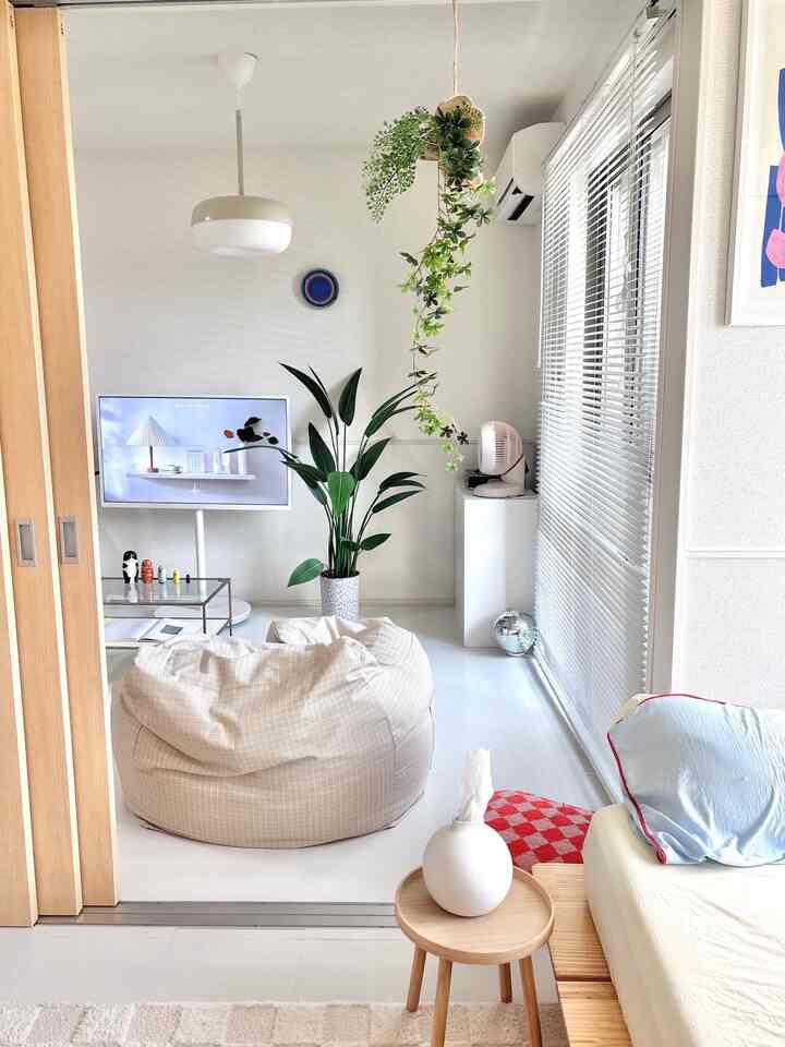 ホワイトとベージュのトーンのリビング、中央にビーンバッグソファとテレビ台、大きな植物が配置されたシンプルモダンな空間