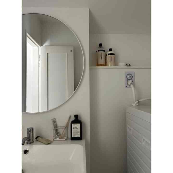 白を基調としたバスルーム、丸い鏡と洗面台が配置されたシンプルで清潔感のあるインテリア