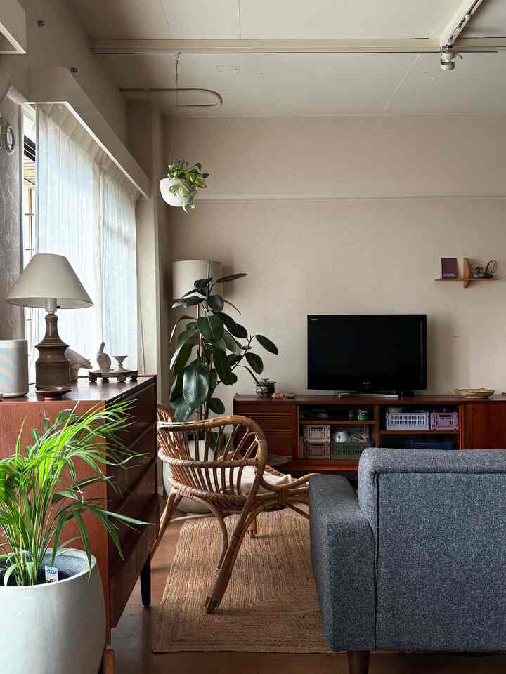 A natural-toned studio apartment living room with brown wood tones and gray sofa, featuring a rattan chair and vintage cabinet