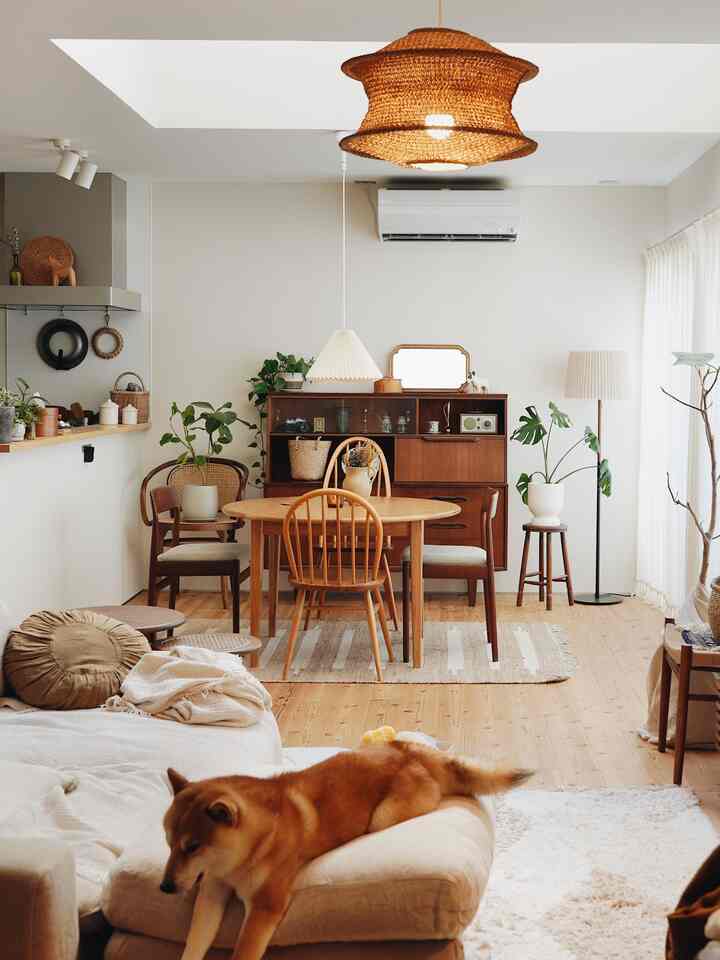 ナチュラルな色調のリビングとダイニング、木製家具とオットマンに犬がくつろぐ雰囲気のあるインテリア