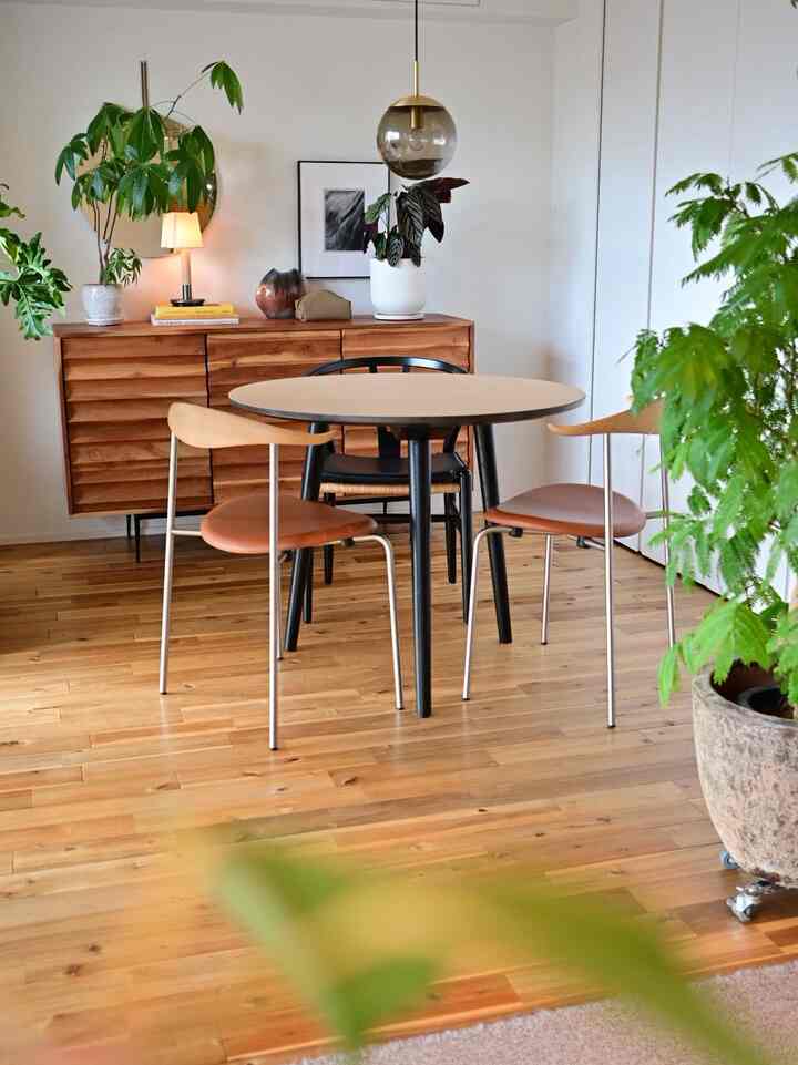 Natural color wood-tone dining room featuring round dining table and chairs, pendant light, and various plants creating a warm atmosphere