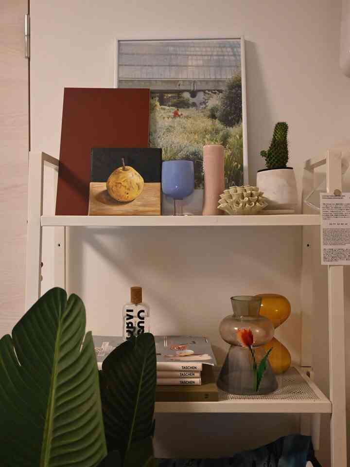 ホワイトのメタル棚に植物や額縁、陶器の装飾品が置かれたナチュラルカラーのインテリア