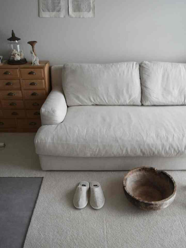 ホワイトとナチュラルカラーのリビング、シンプルなソファと多機能な木製収納が配置された雰囲気のあるインテリア