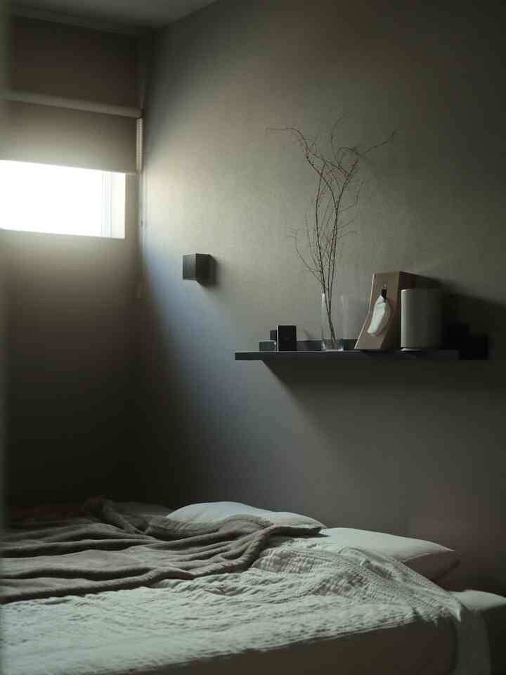 Gray-toned bedroom with black shelf mounted on wall and a bed featuring pillows and beige blanket, creating a calm atmosphere