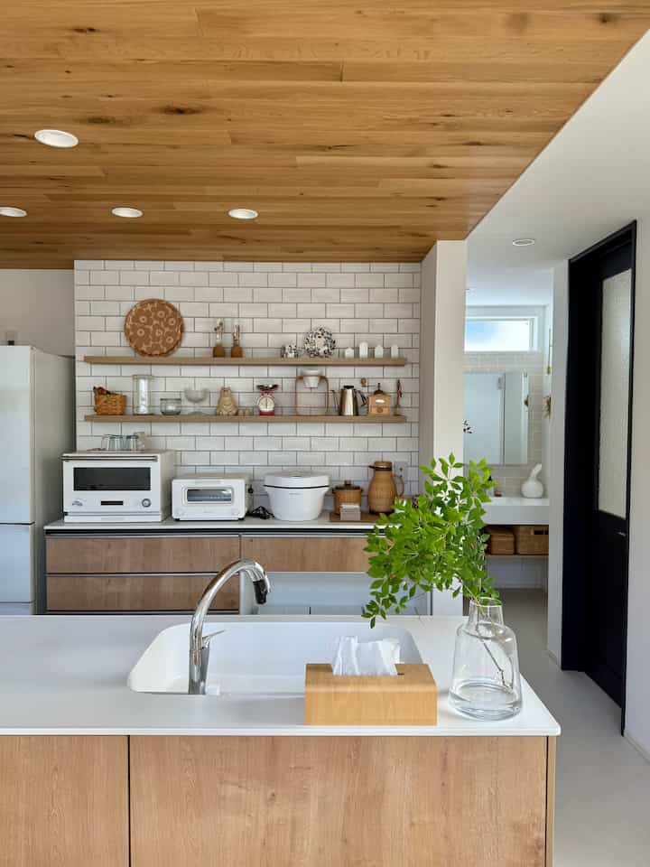 ナチュラルな木目調とホワイトタイルのキッチン、棚に調理器具が並ぶ清潔感のある空間