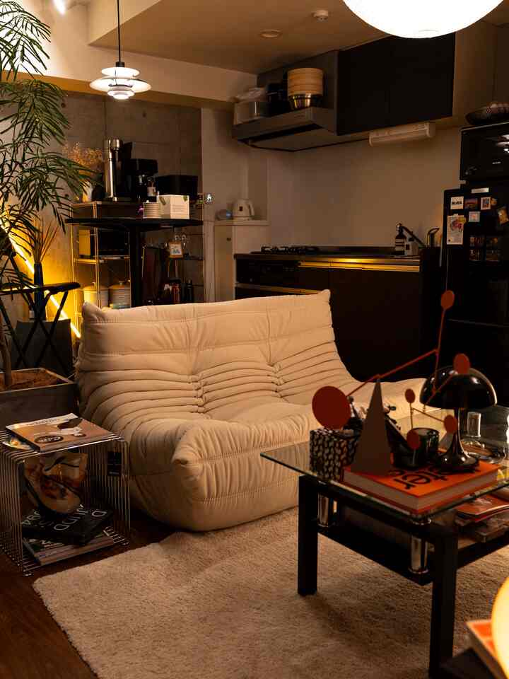 暖かいナチュラルトーンの小型アパートのリビングとキッチン、ふかふかのアイボリーソファとペンダントライトが配置された雰囲気ある空間