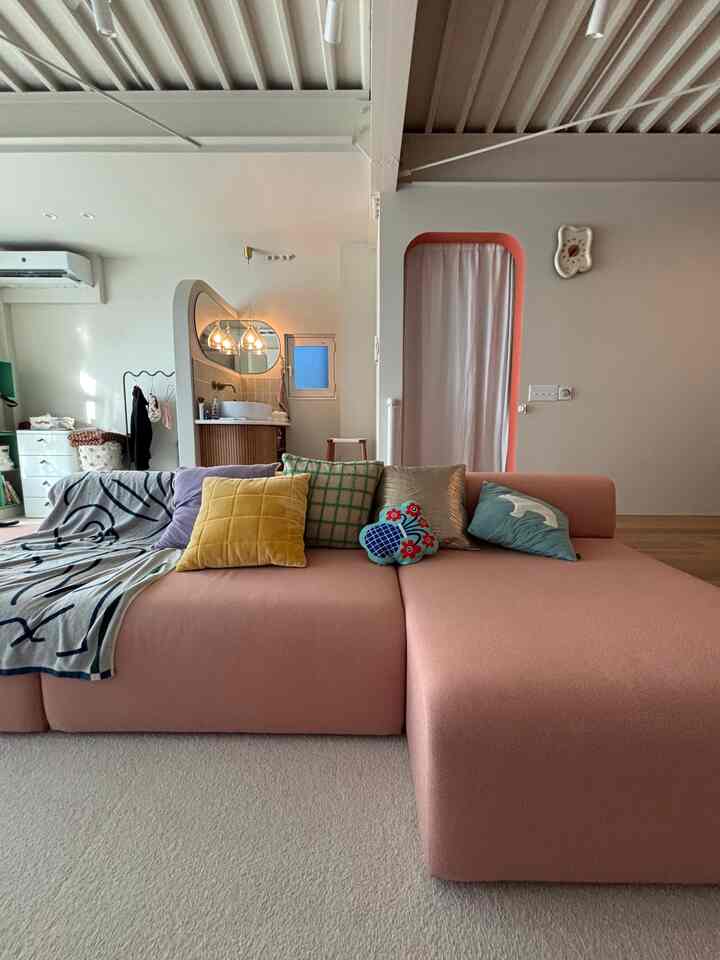 Natural modern living room with a pink sectional sofa and multiple cushions, soft-toned arched doorway and wall clock create cozy ambiance