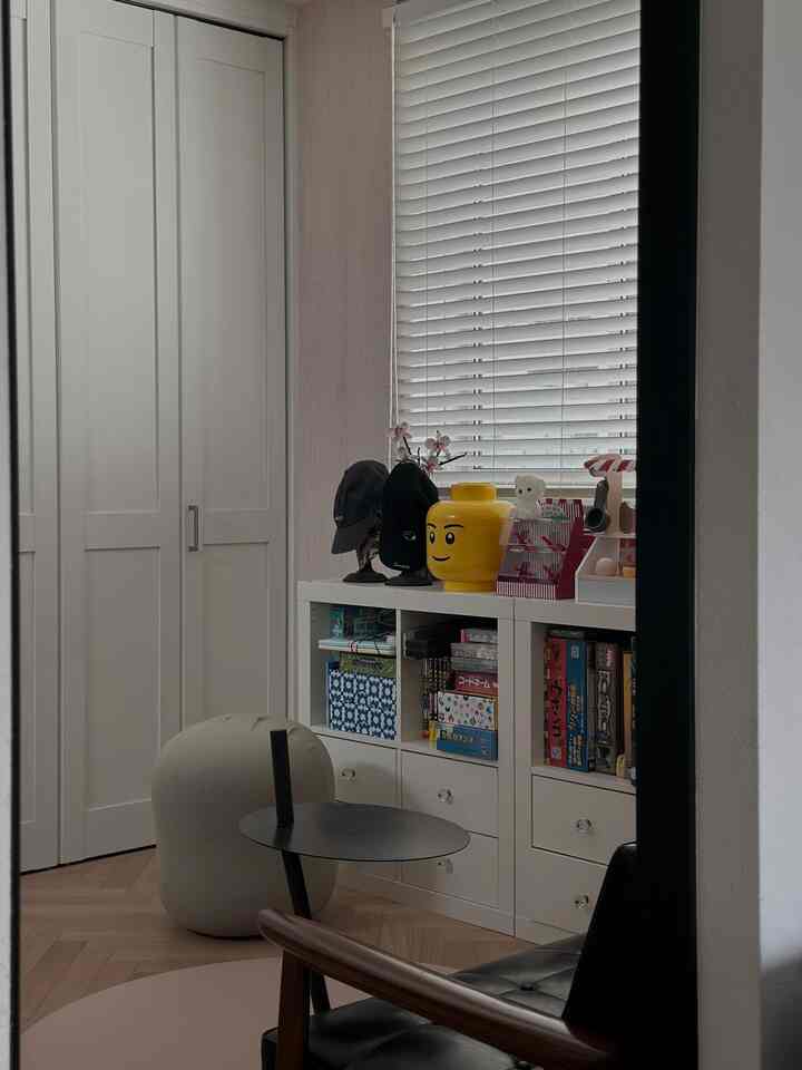 白を基調とした子供部屋、白い壁と収納棚におもちゃとブラインドが配され、清潔感のある空間