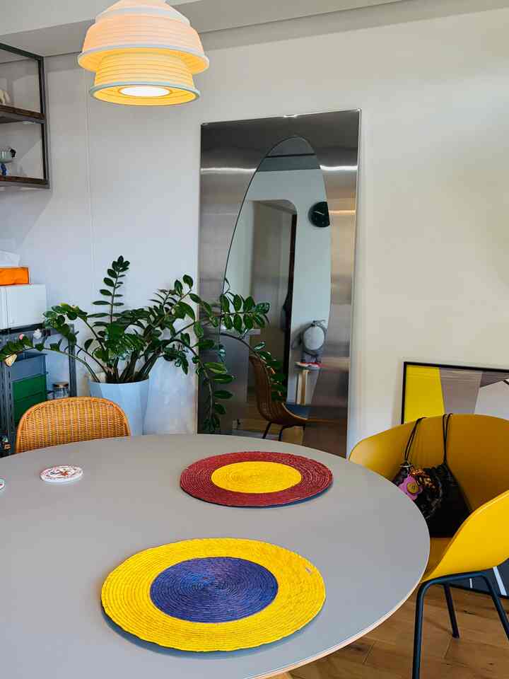 グレーの丸テーブルと黄色い椅子が配置されたダイニングルーム、全身鏡と植物が空間を広く見せる自然な雰囲気のインテリア