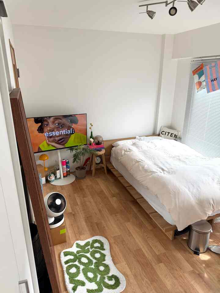 White and wood-tone 1K bedroom featuring a wooden bed frame and wall-mounted TV on left, cozy atmosphere