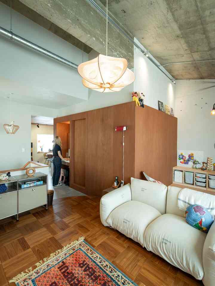 ナチュラルな木目調とクリーム色のソファが置かれたミッドセンチュリーモダンのリビングルーム、コンクリートの露出天井と特徴的な木製の間仕切りが印象的な洗練された空間