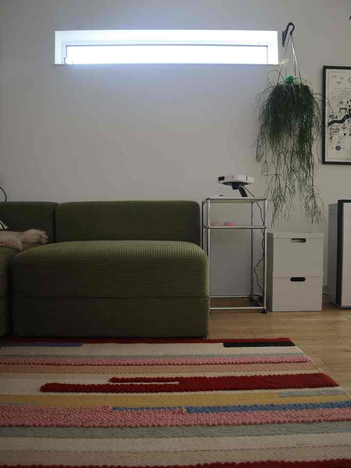 ナチュラルカラーとウッドトーンのリビング、オリーブグリーンのL字型ソファとプロジェクターが配置された清潔感のある雰囲気のあるインテリア