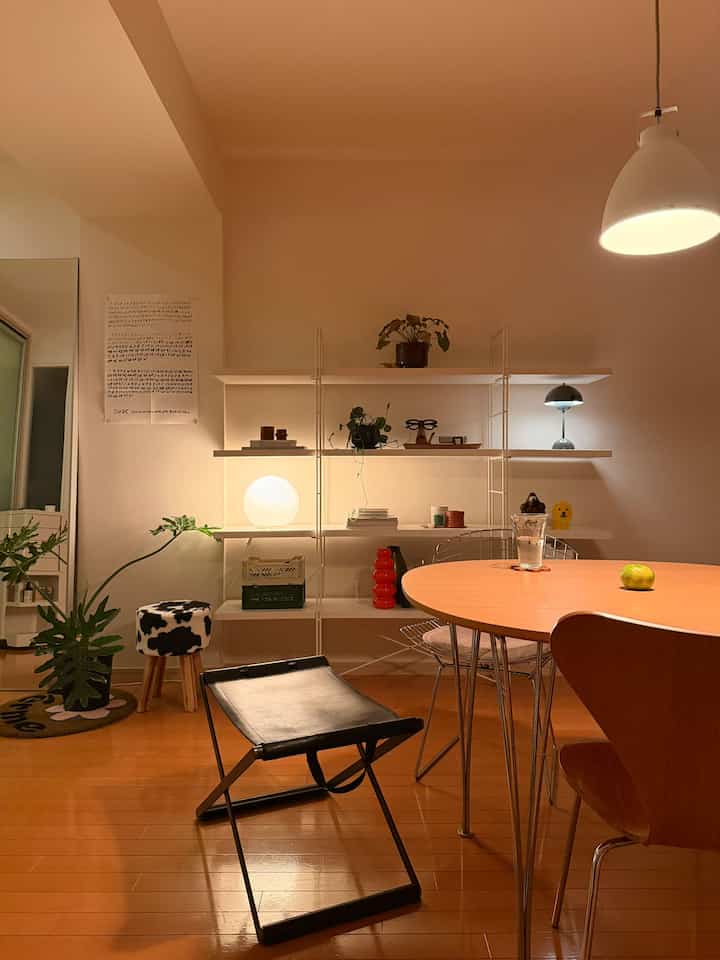 A cozy mid-century modern dining room with bright white walls and warm wood tones, featuring simple shelving and various lighting fixtures