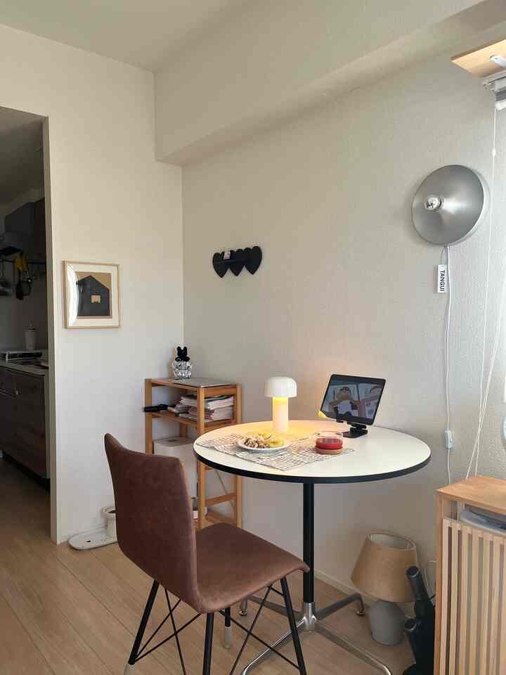 ナチュラルな木目調と白を基調とした1LDKのダイニングスペース、小さな円形テーブルと茶色の椅子が配置されたシンプルなインテリア