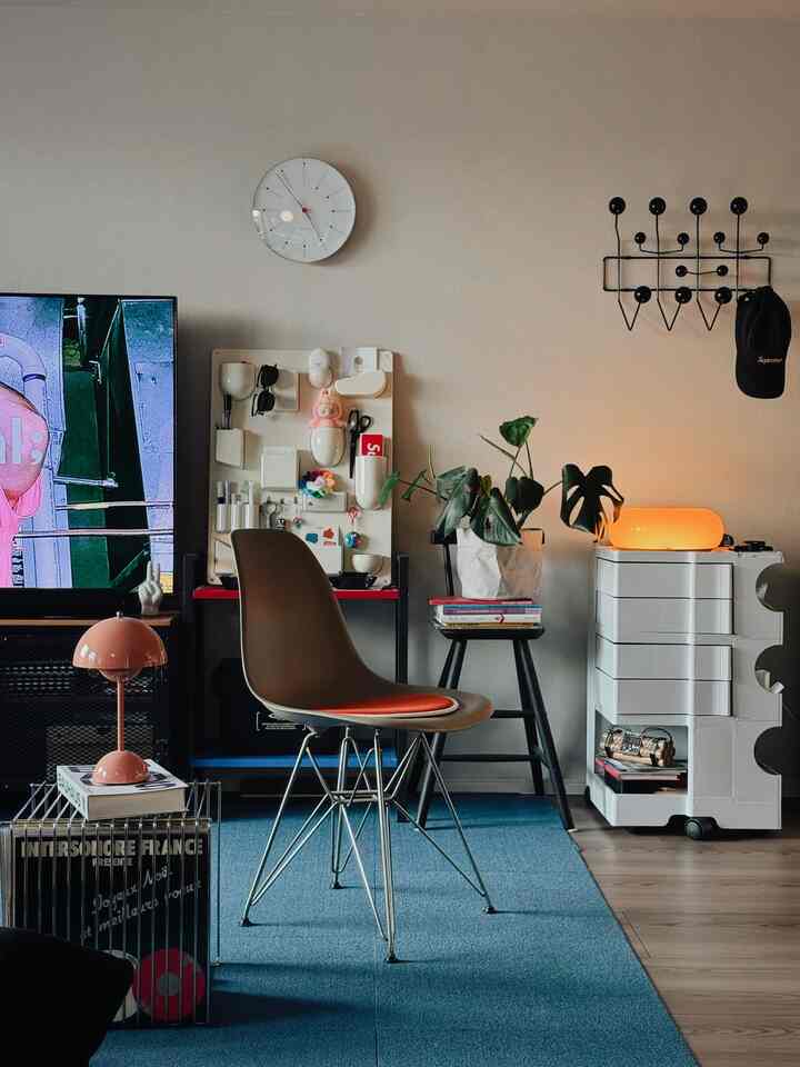 ホワイトとベージュの壁、ブルーのカーペットがあるリビングルーム、中央に椅子と植物が配置された雰囲気のある空間