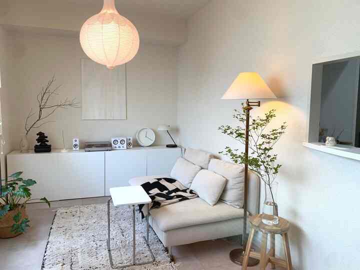 白とナチュラルカラーのリビング、ベージュのソファとフロアランプ、植物が配置された雰囲気のある空間