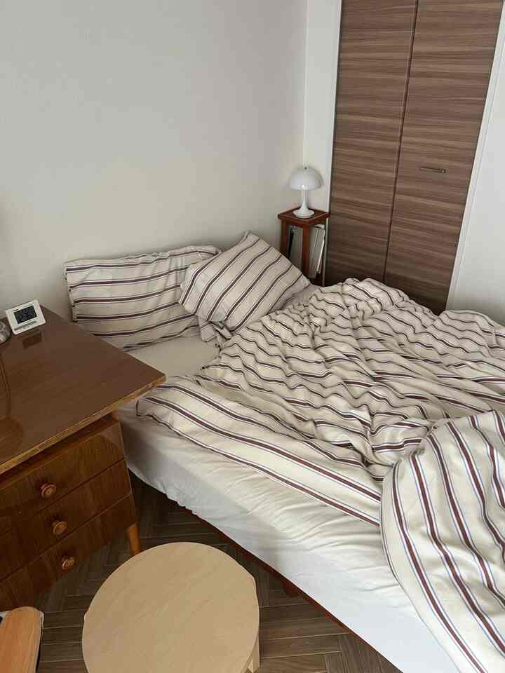 白い壁と木目調の家具が調和した北欧風の寝室、ストライプ柄の掛け布団カバーが置かれた落ち着いた空間