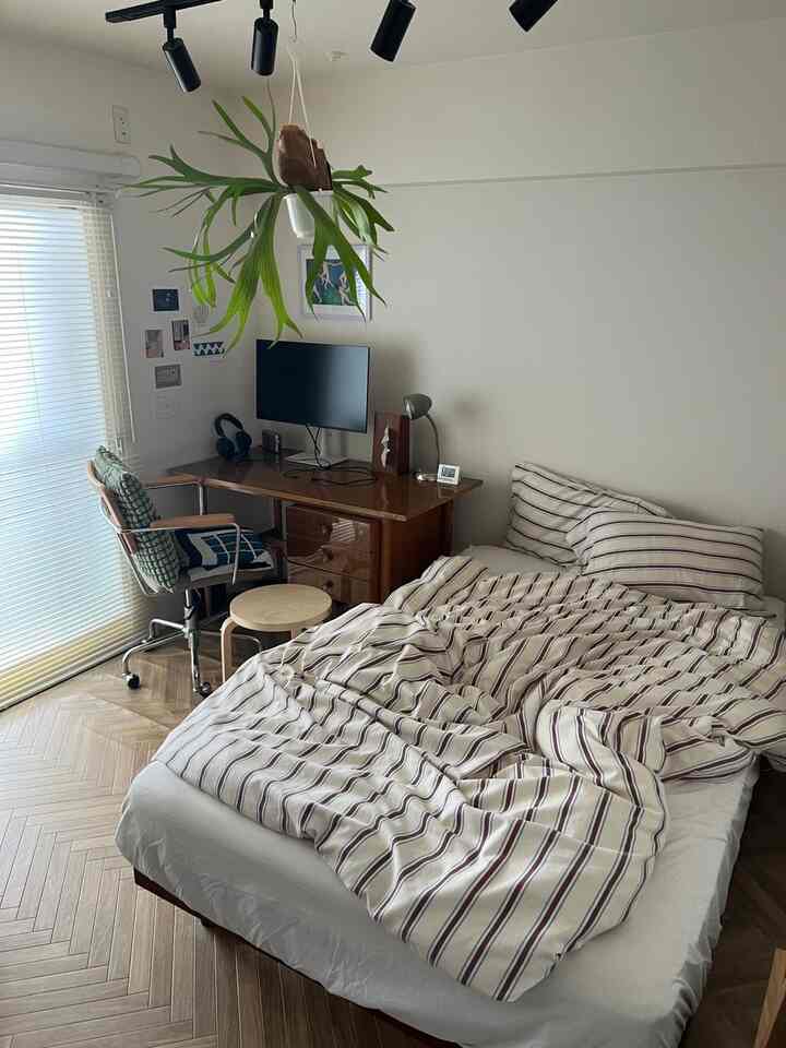 White-walled bedroom with wood tone flooring for a single household, featuring a desk with a computer monitor and minimal furniture layout