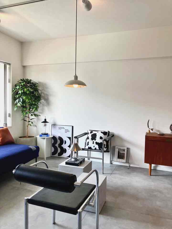 White-walled and gray-floored living room featuring mid-century modern furniture and a pendant light, creating a modern inorganic space
