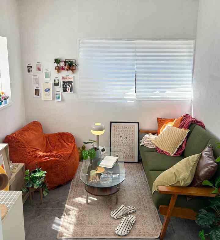 Natural tone living room with a green sofa and an orange bean bag arranged by the window