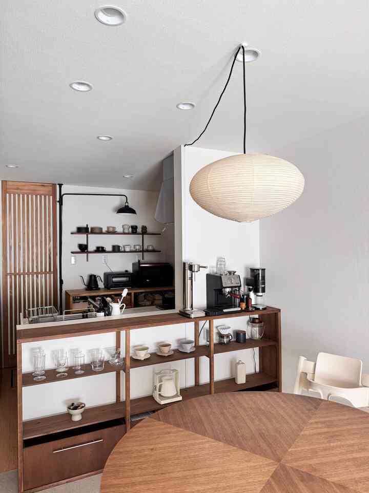 White walls and wood tone dining table with shelving create a cozy dining and kitchen space featuring a child's chair and coffee equipment in a home cafe style