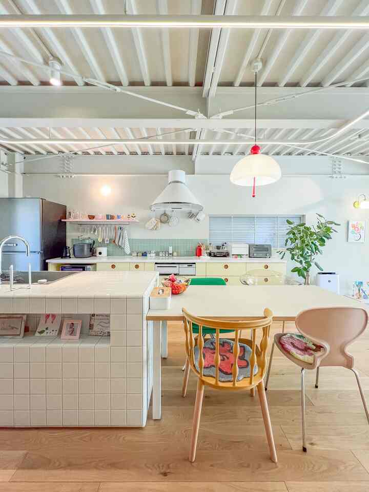 白と木目調が調和するダイニングスペース、パステルカラーの椅子が配置された明るいモダンなキッチン
