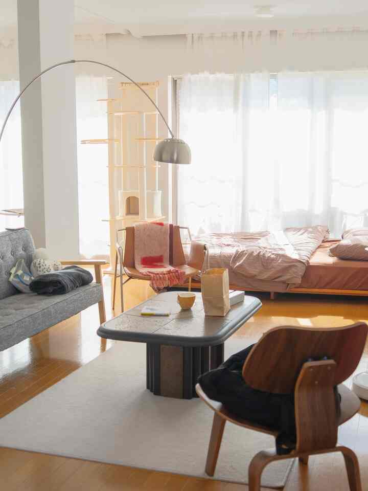 白いカーテンと木目調の床があるリビング、中央にキャットタワーとアームチェア、ラグが配置されたモダンで温かみのある空間