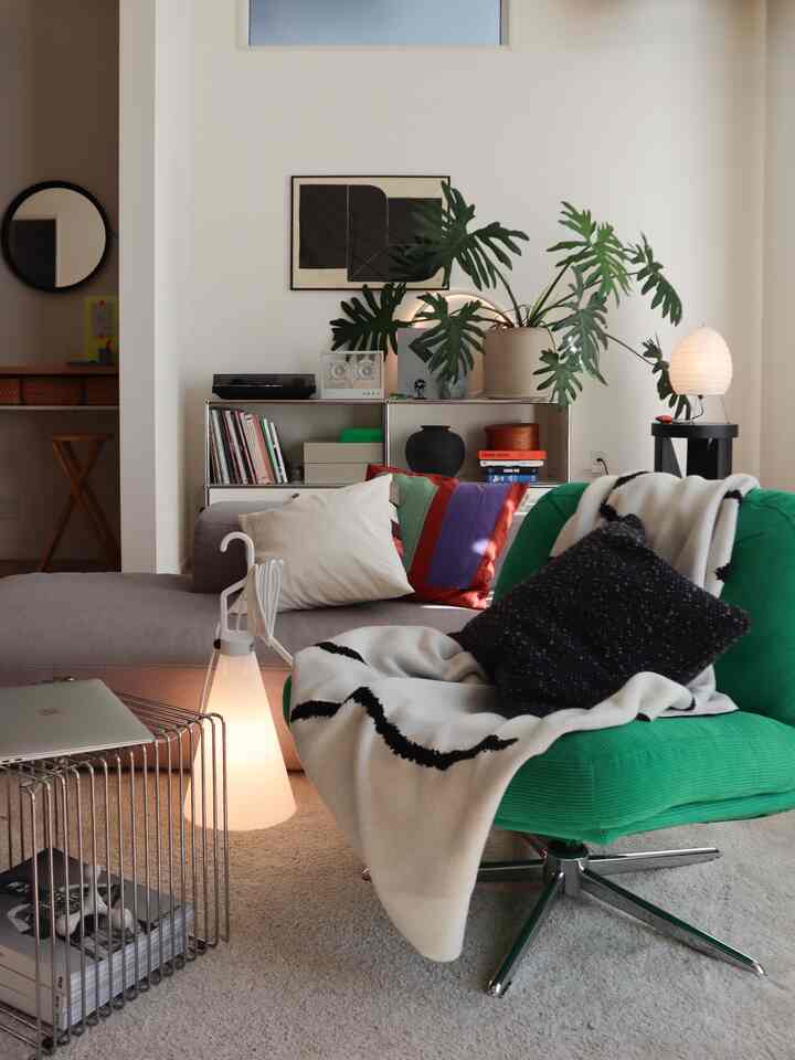 カラフルなクッションと緑のアームチェアがあるモダンなリビング、ライトベージュのカーペットと大きな植物が自然な雰囲気を演出