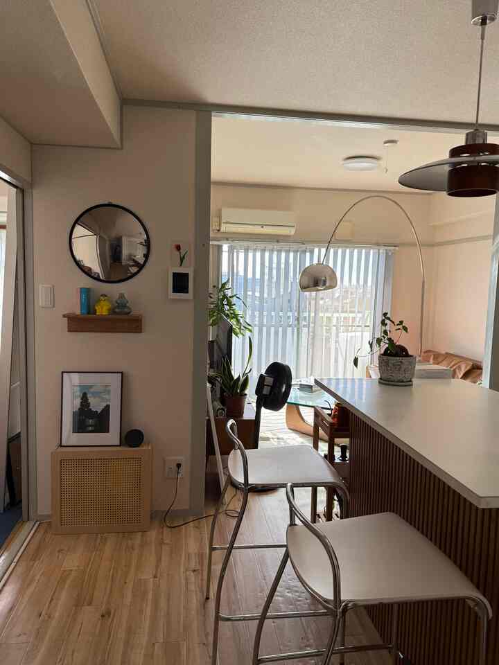 Bright living and kitchen space in white and wood tones featuring an arched floor lamp and bar stools with a cozy atmosphere