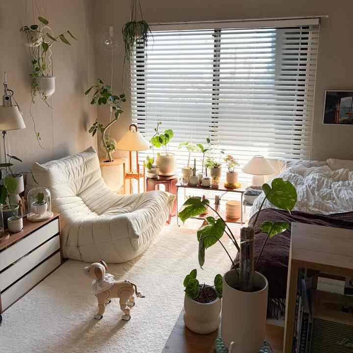White and natural toned living room featuring an ivory sofa and many plants near the window creating a cozy atmosphere