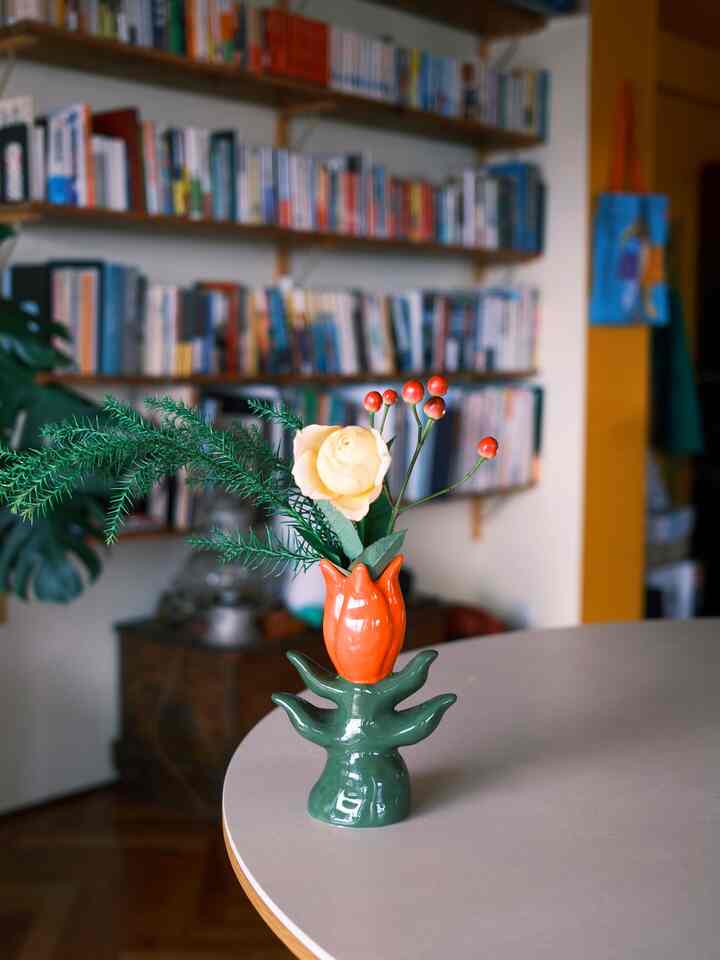 オレンジとグリーンの花瓶が置かれたナチュラルなダイニングルーム、書棚と植物が調和したシンプルな雰囲気のインテリア