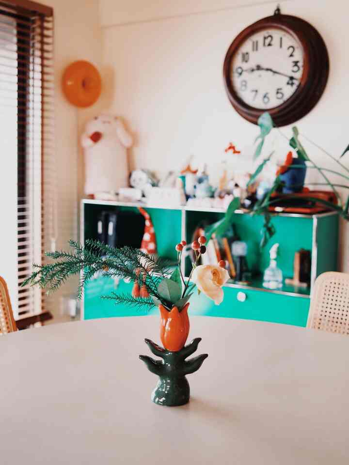 白と緑の色調のダイニングルーム、中央に個性的な花瓶が置かれたテーブル、背景には壁掛け時計とキャビネットがある雰囲気のあるインテリア