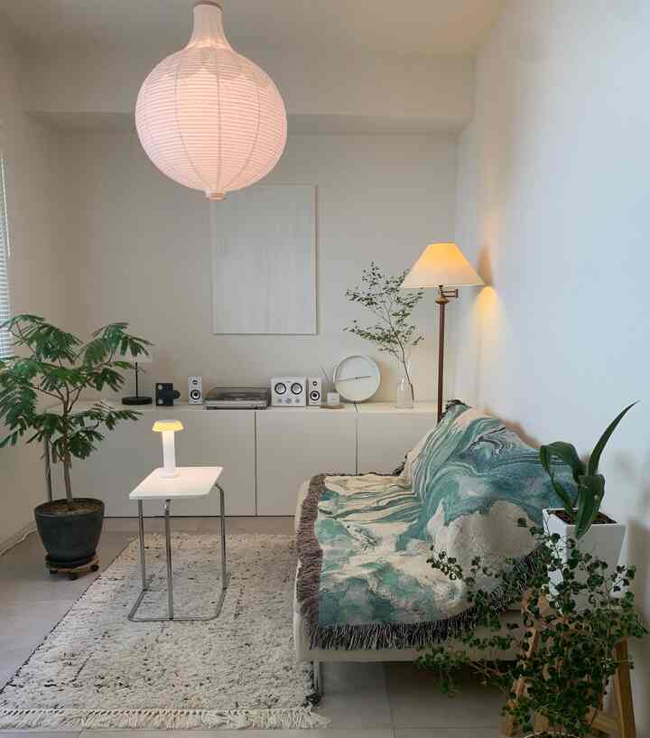 白を基調としたナチュラルカラーのリビング、ソファにブランケットが掛けられ、植物が配置された落ち着いた雰囲気のインテリア